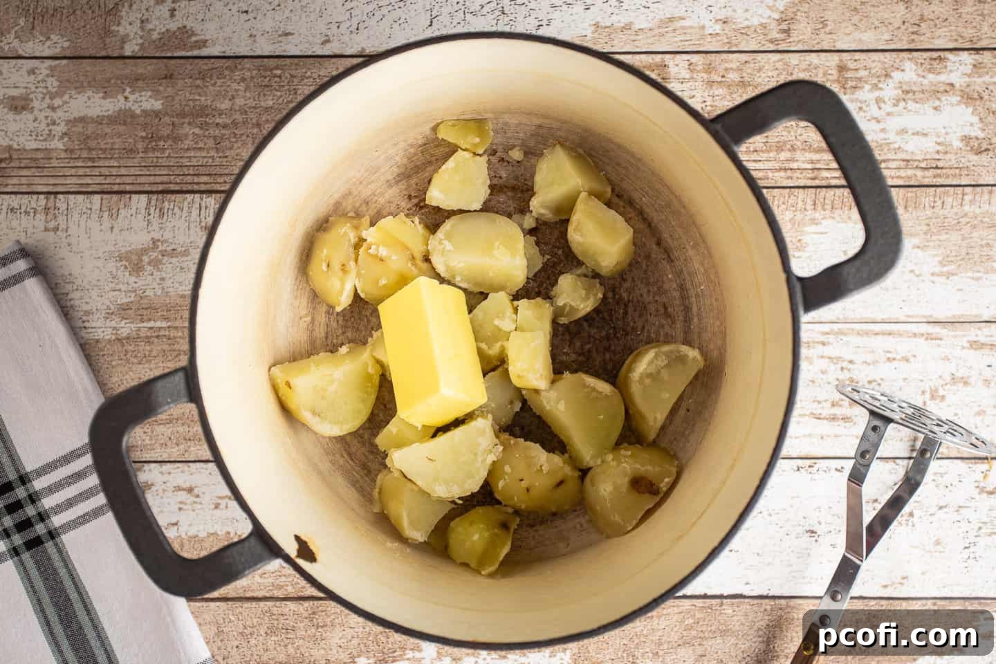 Boiled and drained potatoes in a pot, with cubes of unsalted butter melting on top, ready for mashing.