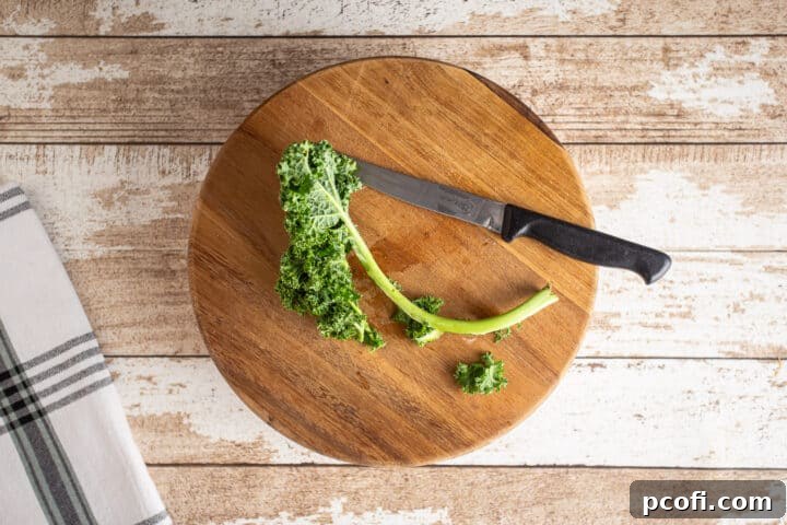 Hands demonstrating how to remove the tough central stem from a kale leaf, preparing it for chopping.