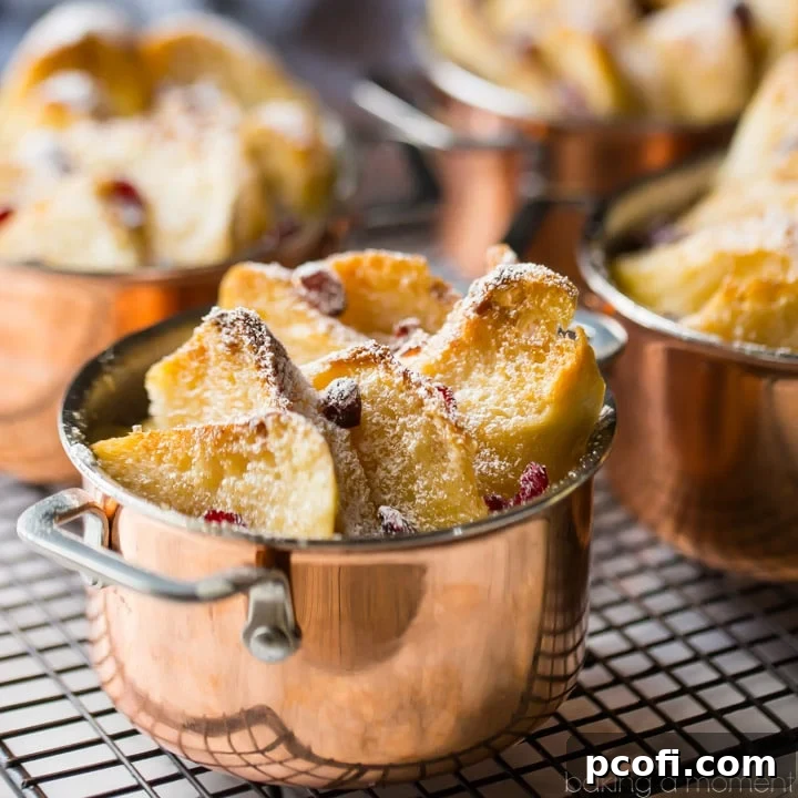 Individual bread & butter puddings, in mini copper pots, with toasty buttered bread, dried cranberries, and powdered sugar, on a wire cooling rack. 