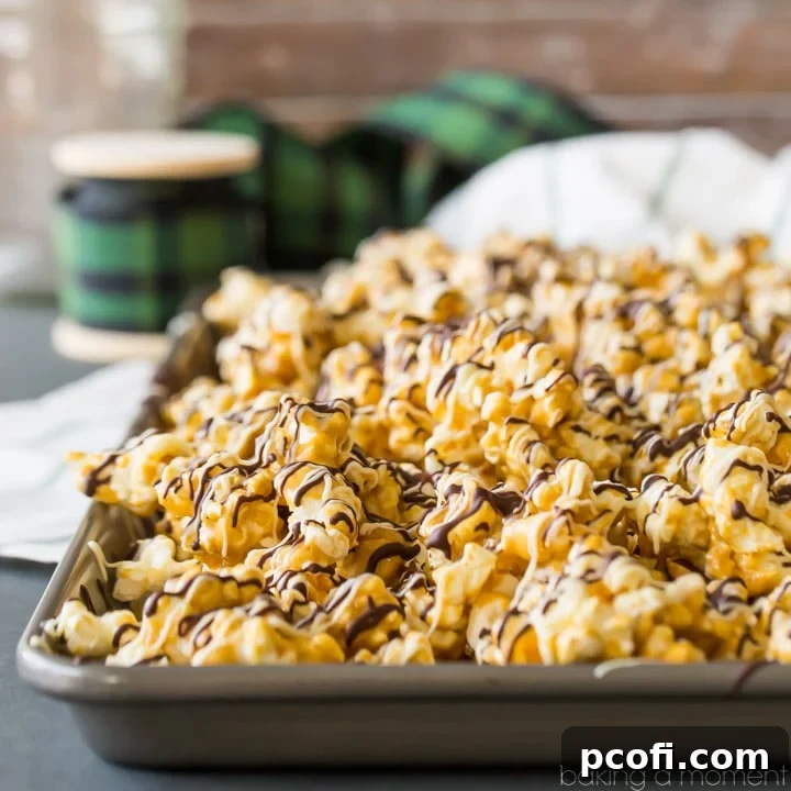 Homemade Moose Munch butter toffee caramel popcorn with nuts and chocolate drizzle, on a baking sheet with a spool of holiday ribbon in the background