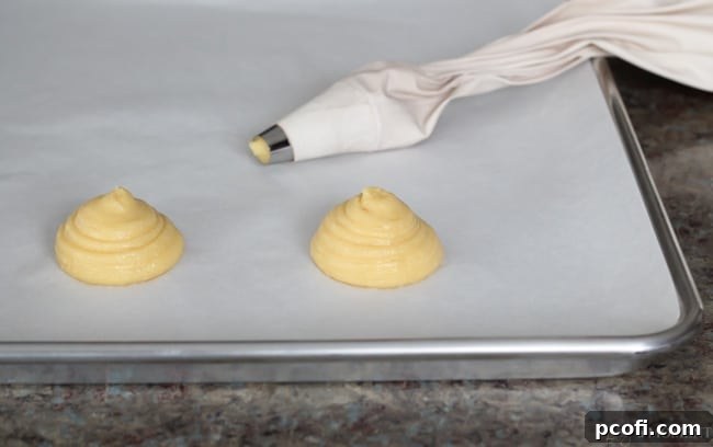 Piped cream puff shells on a parchment-lined baking sheet before baking