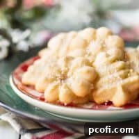 An assortment of buttery spritz cookies, on a red and green plate with holiday greenery in the background.
