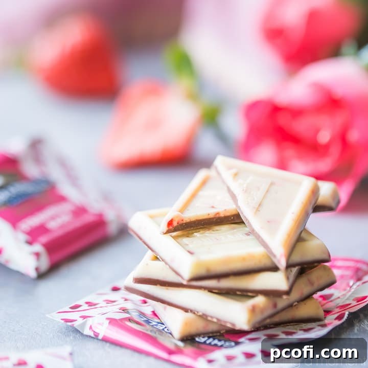 A perfectly stacked pile of Ghirardelli Strawberry Bark SQUARES, set against a romantic backdrop of fresh roses, ripe strawberries, and elegant candy wrappers, highlighting their appeal as a thoughtful gift.