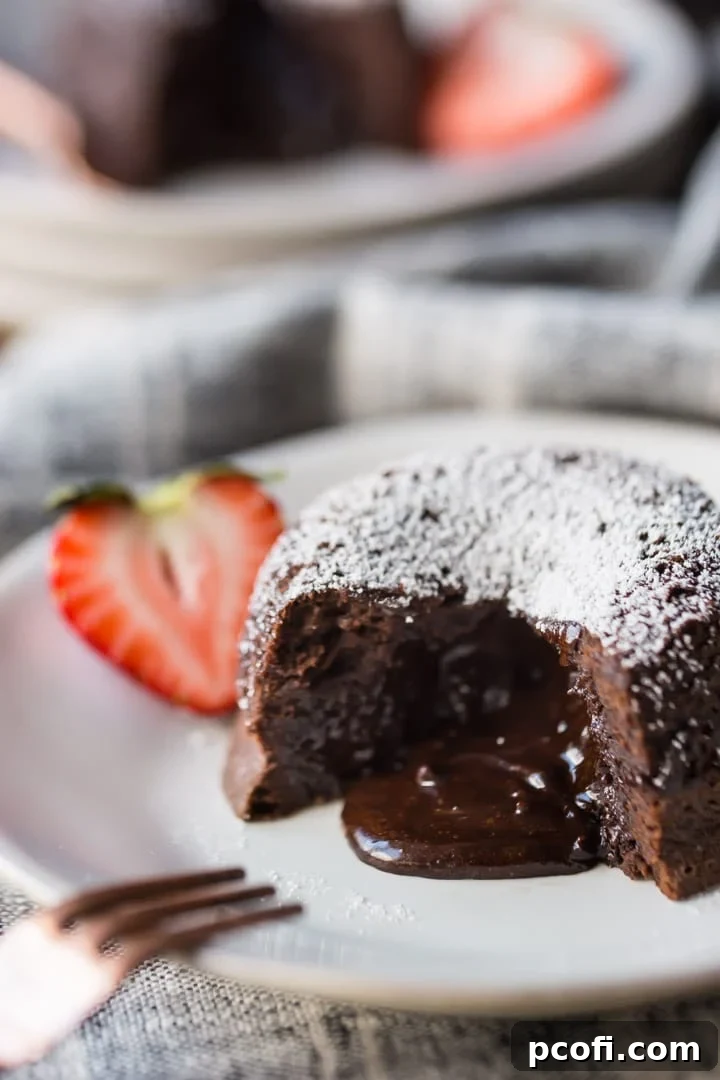 Chocolate Molten Lava Cake on a white plate, with liquid chocolate spilling from the center. Garnished with a strawberry, and a linen cloth beneath the plate and a copper fork on the side.
