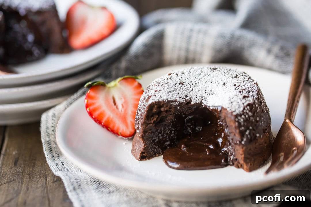 Chocolate Molten Lava Cake on a white plate, with liquid chocolate spilling from the center. Garnished with a strawberry, and a linen cloth beneath the plate and a copper fork on the side.