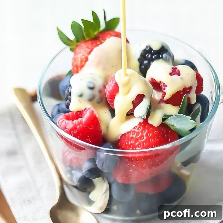 Creme Anglaise: rich, velvety vanilla custard sauce being poured over a bowl of berries, sitting on a linen napkin with a gold spoon off to one side.