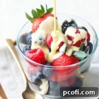 Creme Anglaise: rich, velvety vanilla custard sauce being poured over a bowl of berries, sitting on a linen napkin with a gold spoon off to one side.