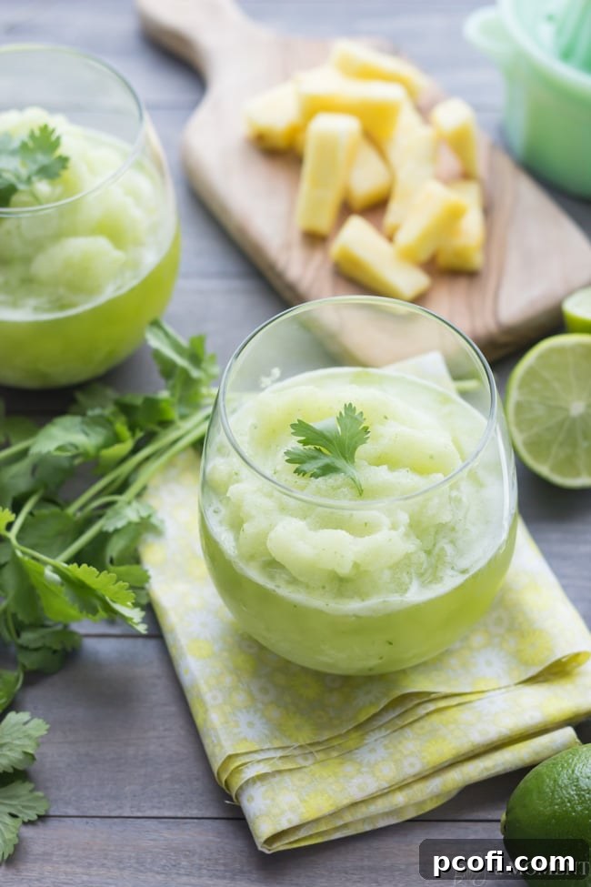 A tall glass of Frozen Pineapple Cilantro Mojito, showcasing its frosty texture and the vibrant green of fresh cilantro leaves within. | Baking a Moment