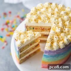 Triple layer rainbow fruity pebble cake with gold sprinkles, with a slice cut out and fruity pebbles scattered on a light gray background.