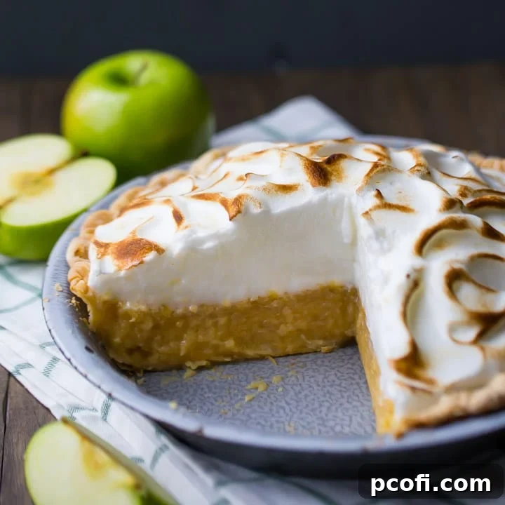 A beautifully baked Irish apple amber pie, showcasing its golden meringue topping and a glimpse of the apple filling, set against a dark background with fresh green apples.