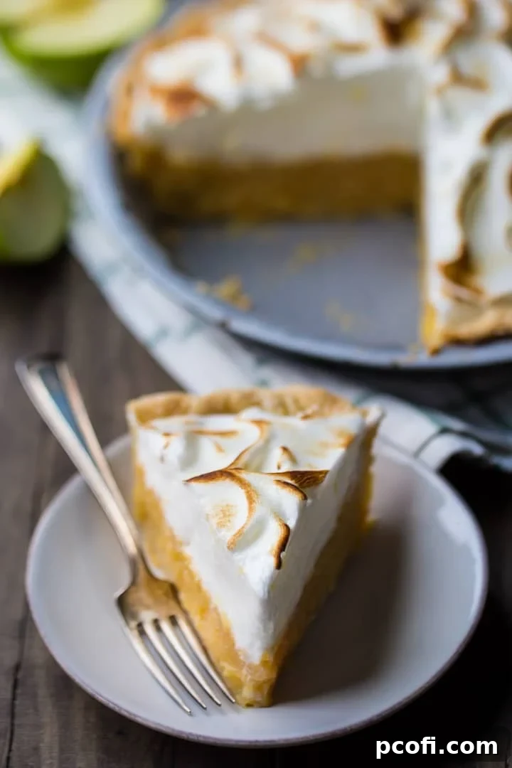A close-up shot of a slice of Irish apple amber on a plate with a silver fork, showing the distinct layers of meringue, apple filling, and crust. The full pie with a slice missing is visible in the soft background.