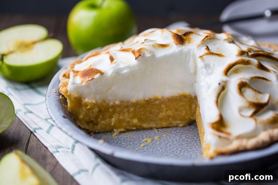 A detailed close-up of Irish apple amber with a slice removed, highlighting the texture of the meringue and the apple filling, with fresh green apples blurred in the background.