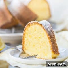 A tall slice of buttery lemon pound cake on a white plate over a yellow napkin, with a silver fork alongside.