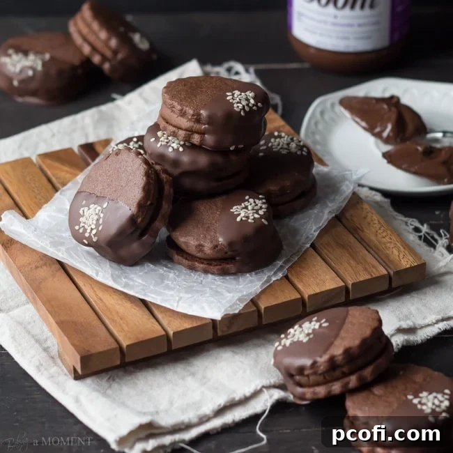 Decadent Chocolate Sesame Butter Sandwich Cookies with dark chocolate coating and sesame seeds, on a white plate.