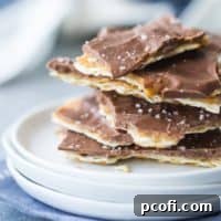 Square image of a stack of matzo toffee on a small white plate, with a blue napkin underneath.