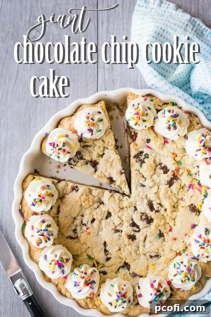 An overhead view of a giant chocolate chip cookie cake, garnished with elegant buttercream rosettes and a colorful scattering of rainbow sprinkles.