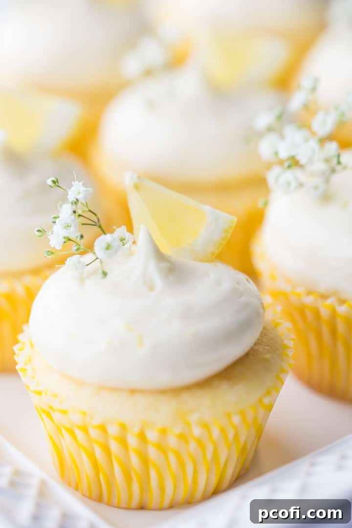 Vertical image displaying a beautiful arrangement of lemon cupcakes with lemon curd filling and lemon cream cheese frosting, elegantly garnished with lemon wedges and delicate baby's breath.