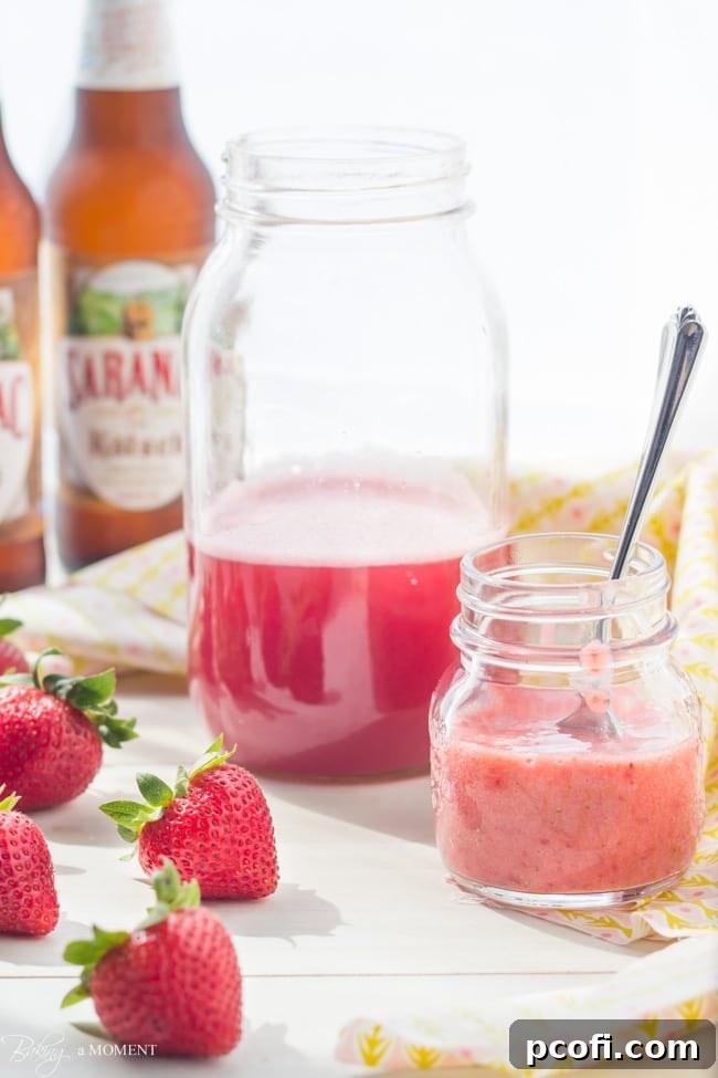Fresh ingredients for Strawberry Rhubarb Shandy, including strawberries, rhubarb syrup, and a bottle of beer, laid out on a rustic surface.