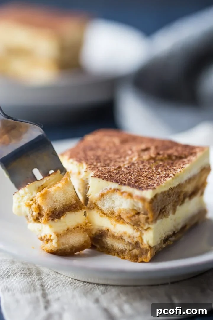 A fork lifts a bite from a perfect slice of tiramisu, showcasing its creamy layers and delicate texture.