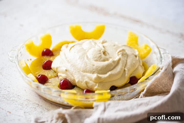 Pineapple upside-down cake batter being poured over the pineapple and cherry topping in the baking pan.