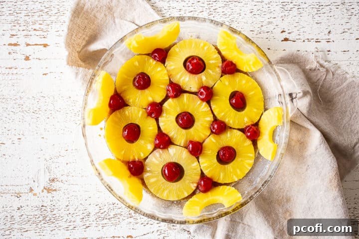 Pineapple slices and maraschino cherries arranged decoratively at the bottom of a cake pan over the brown sugar mixture.
