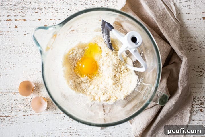 Adding a single egg to the developing cake batter in a mixer.