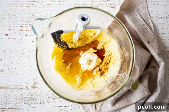 Wet ingredients including sour cream, pineapple juice, and vanilla extract being added to the cake batter.