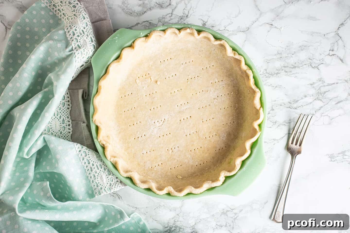 A docked, unbaked pie crust in a green pie dish.