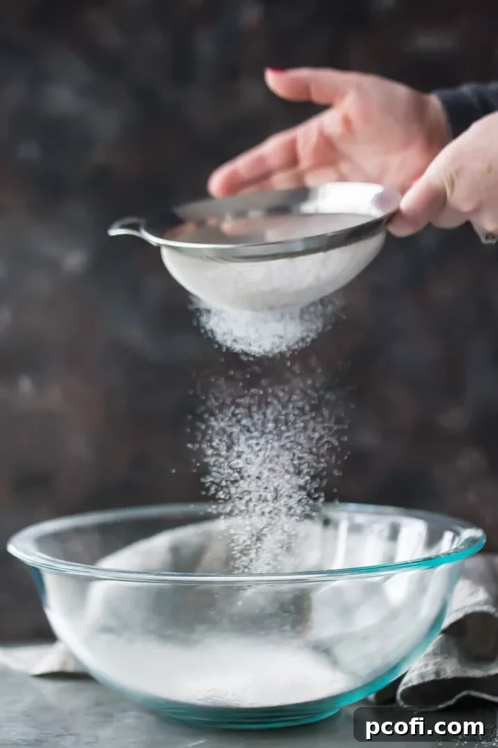 A graceful vertical image of cake flour being meticulously sifted into a clear glass bowl, emphasizing its light and airy quality, crucial for delicate baking.