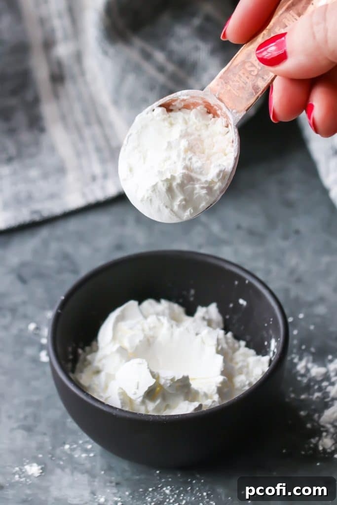 A copper spoon delicately placing white cornstarch into a small brown bowl, illustrating the process of creating a homemade cake flour substitute for tender baking.