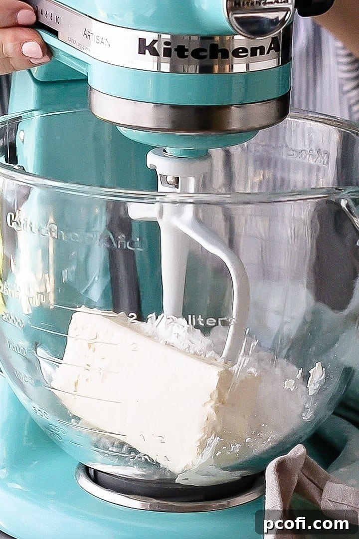 Cold cream cheese and powdered sugar ready to be whipped in a stand mixer bowl, forming the stable base for whipped cream frosting.