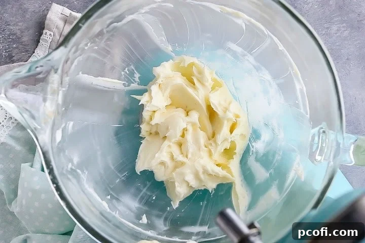Smooth, creamy whipped cream cheese and powdered sugar mixture in a glass mixing bowl, forming the base of the frosting.