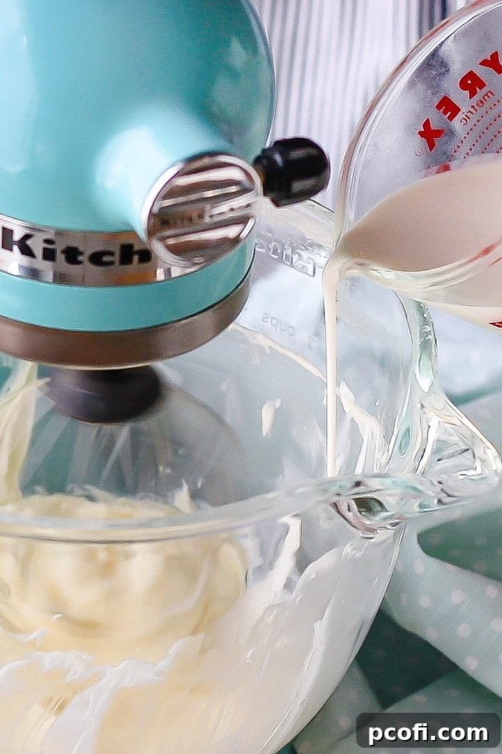 Pouring cold heavy cream slowly into a mixing bowl containing whipped cream cheese, essential for stabilized whipped cream.