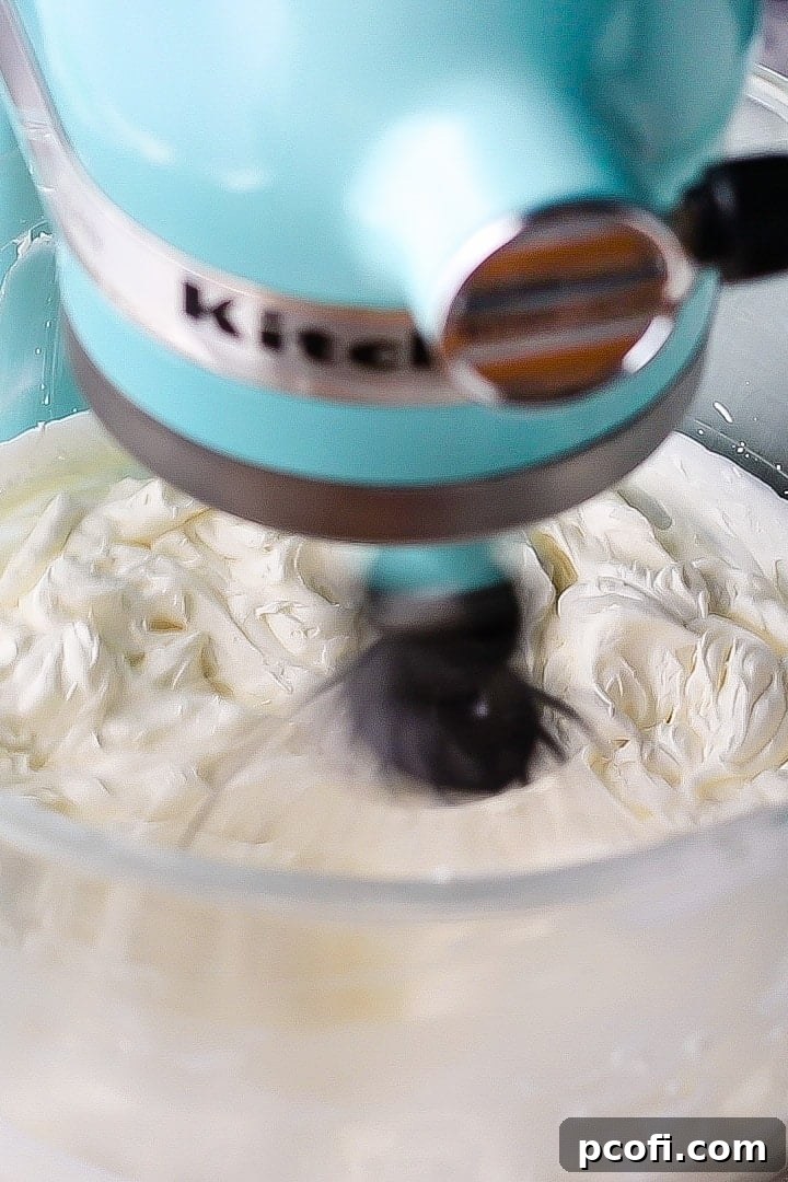 Fluffy cream cheese whipped cream frosting with stiff peaks in a glass mixing bowl, perfectly whipped and ready to use.