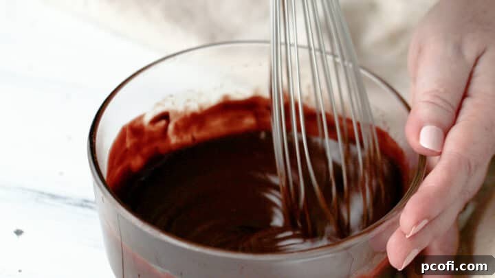 Whisking the chocolate glaze in a glass bowl until it achieves a smooth, shiny consistency.