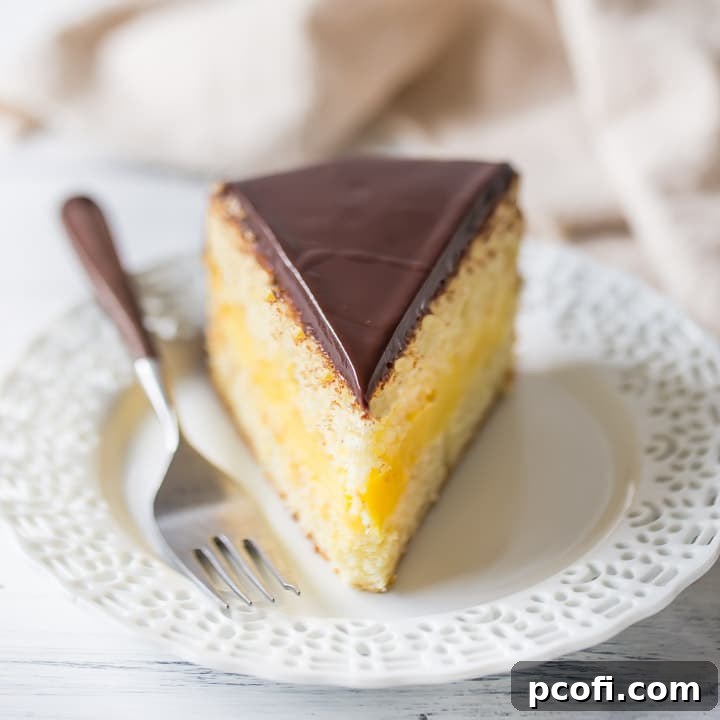 A perfect slice of homemade Boston Cream Pie, showcasing distinct layers of golden vanilla cake, creamy yellow pastry cream, and a glossy dark chocolate topping.