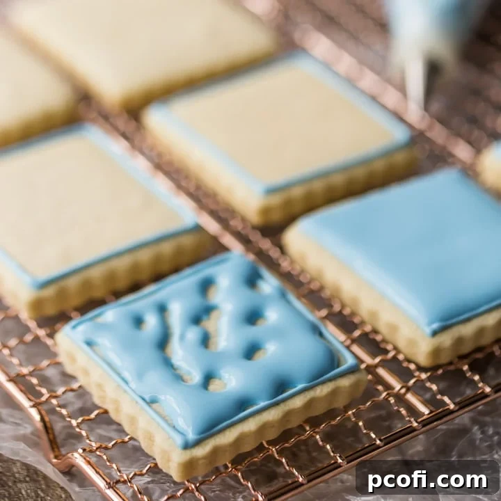 Delicately piped blue royal icing on elegant square cookies arranged on a wire cooling rack, ready for festive occasions or gifting.