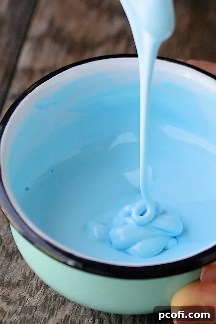 A vibrant close-up of thin, self-leveling blue royal icing expertly prepared for flooding, showcasing its smooth, flowing texture in a bowl.