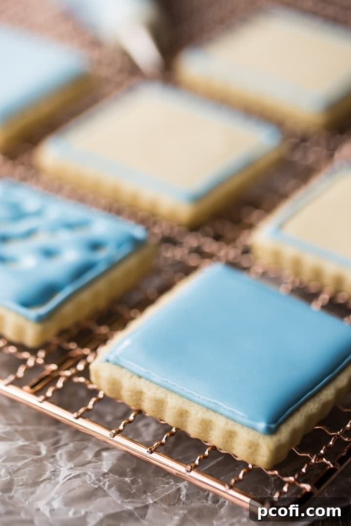 Detailed close-up of a square sugar cookie featuring fluted edges, artfully decorated with stiff royal icing piped as a precise border and thinner, self-leveling flood icing filling the center for a smooth finish.