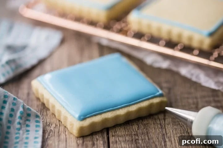 A perfectly smooth, uniformly flooded blue royal icing surface on a square sugar cookie, demonstrating the flawless finish achievable with proper consistency and application.