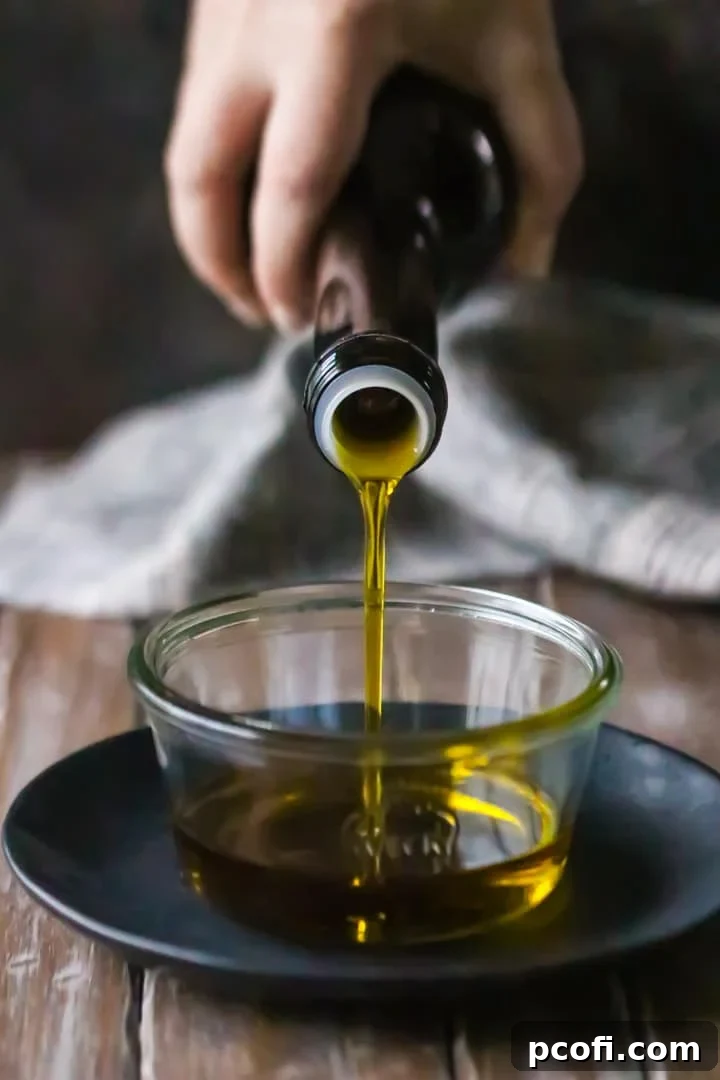 Rich golden olive oil being poured from a bottle into a clear glass dish, ready to be used in a Spanish olive oil cake recipe.