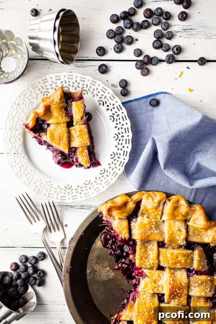 Overhead image of blueberry pie with a slice cut out and plated, with the thick blueberry pie filling spilling out.