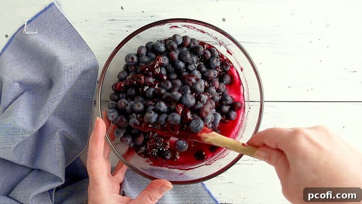 Stirring additional blueberries into cooked blueberry pie filling.