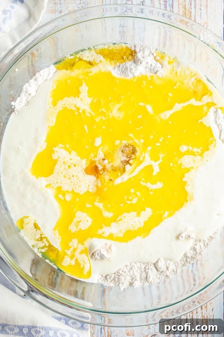 Liquid ingredients like buttermilk, melted butter, eggs, and vanilla being poured into a well created in the dry ingredients for waffle batter.