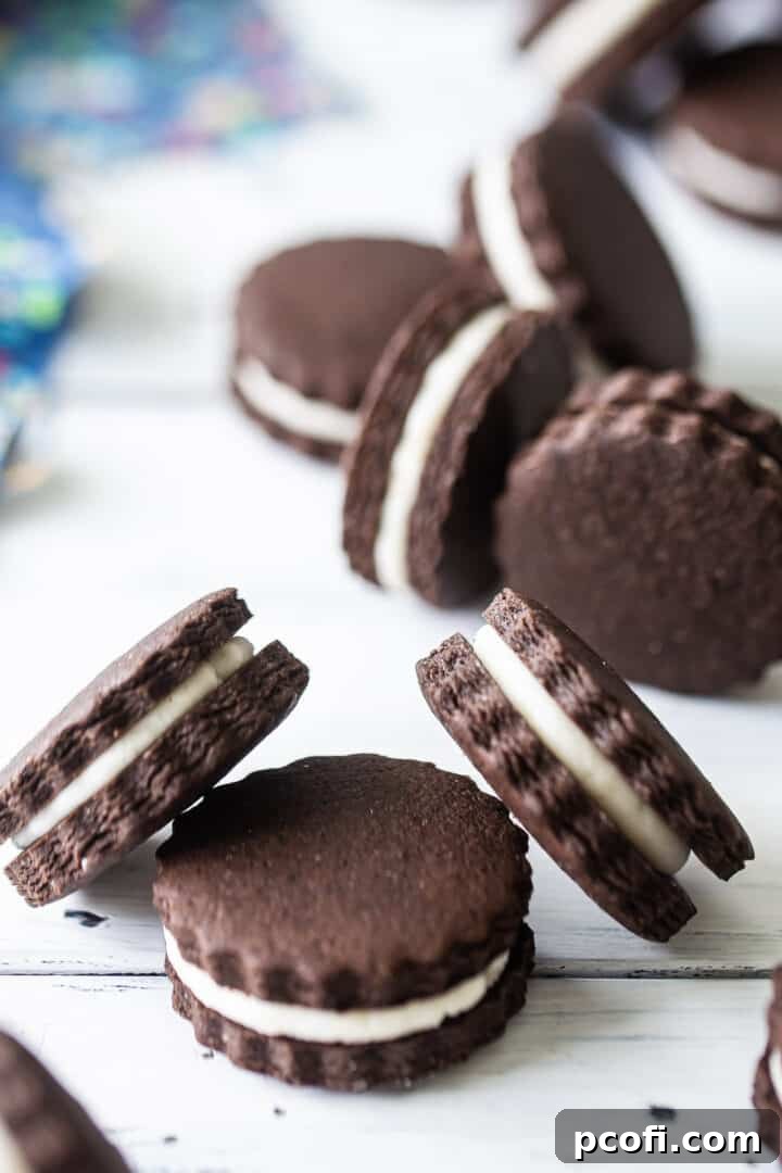 Homemade Oreo cookies tumbling over a distressed white tabletop, emphasizing their appealing texture and dark color.
