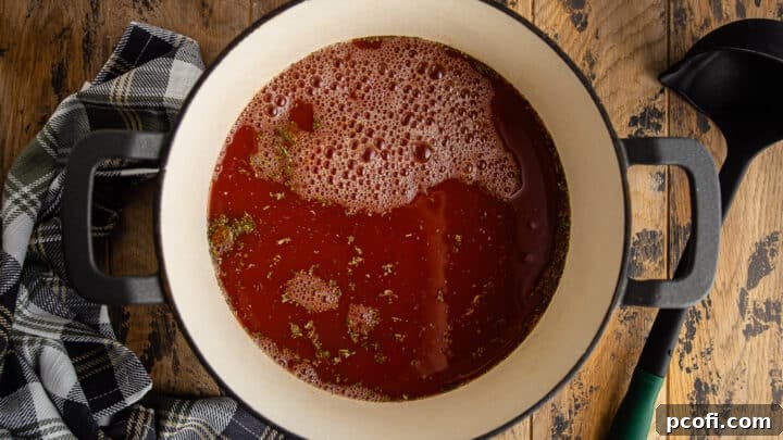 Adding chicken stock to crushed tomatoes and seasonings.