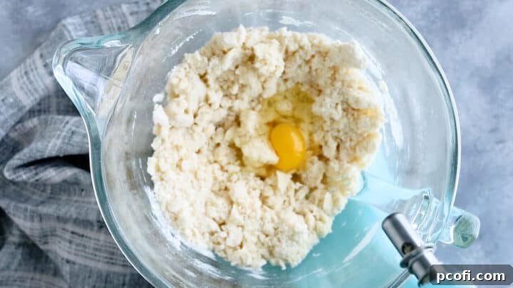 Adding large eggs one at a time into the developing cake batter for smooth incorporation.