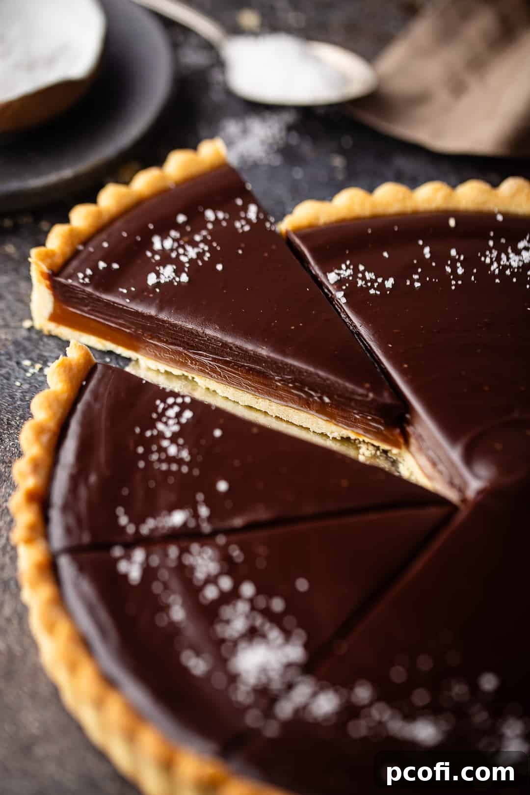 A perfectly portioned slice of salted caramel chocolate tart, set against a dark background, highlighting its rich layers.
