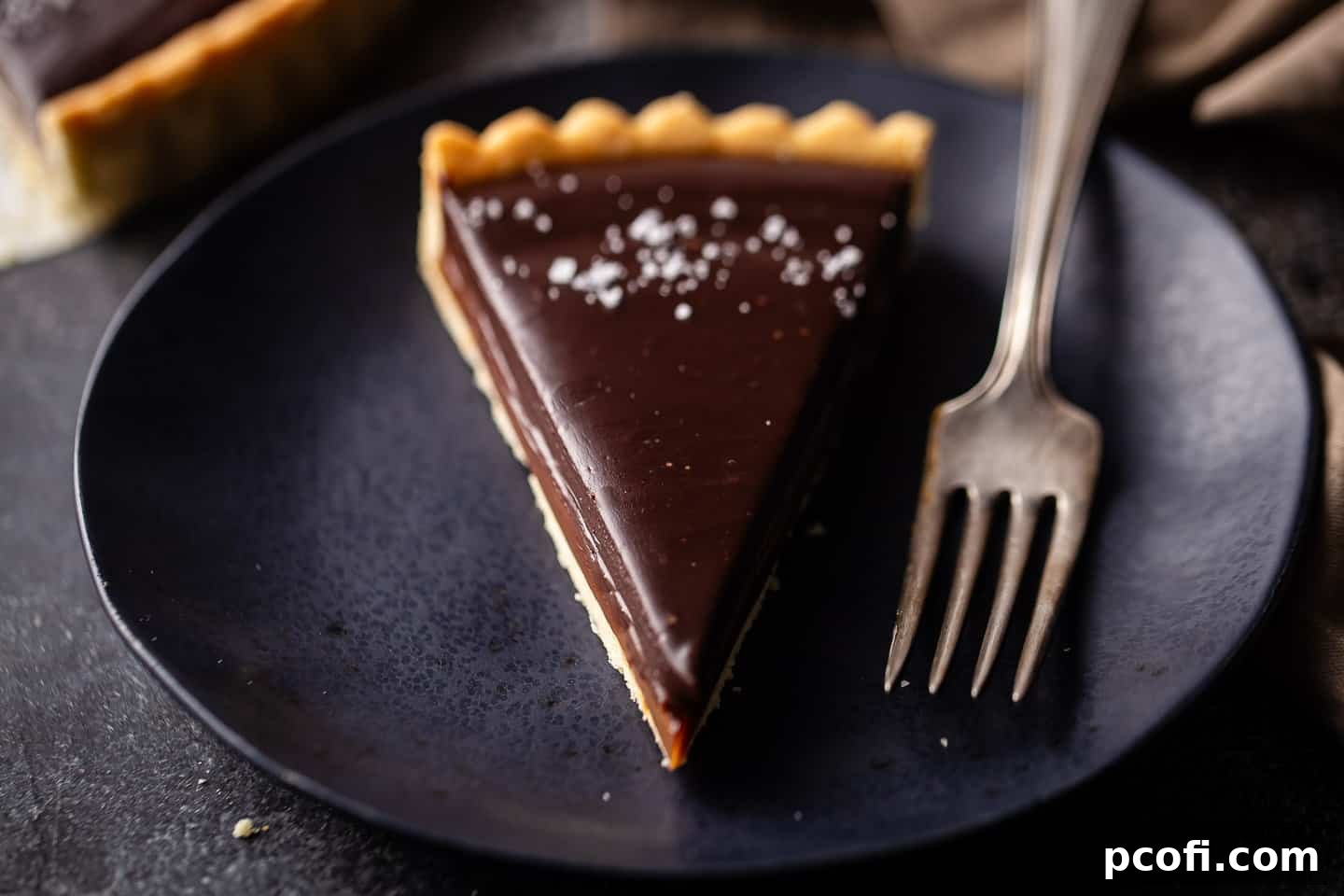 A beautifully presented salted caramel chocolate tart, sliced and garnished with flaky sea salt, ready to be enjoyed.