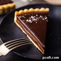 Chocolate caramel tart on a dark blue plate with a vintage silver fork.